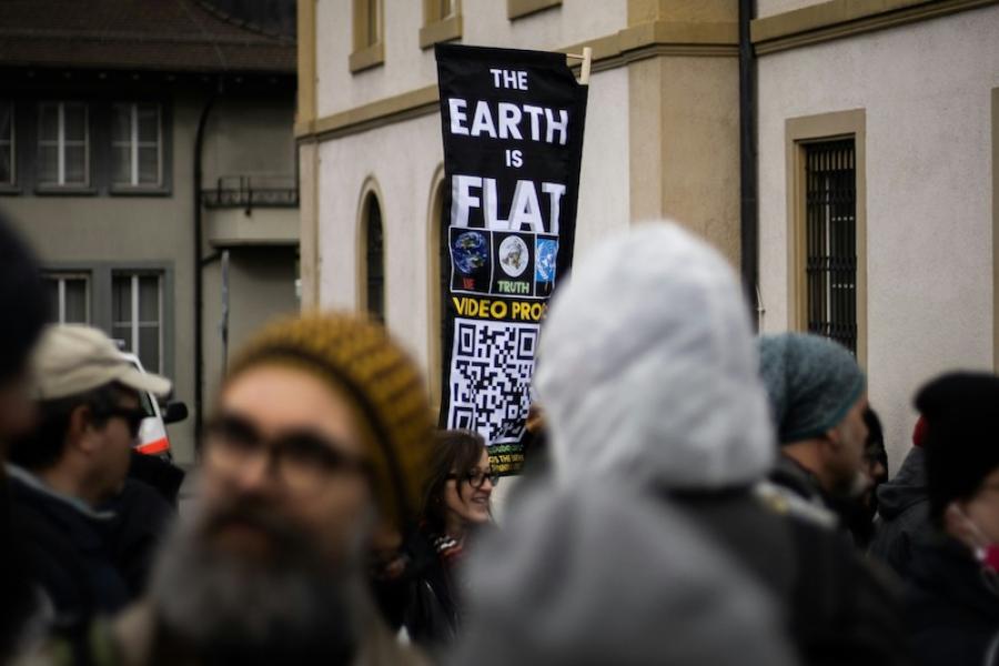 A sign sticks out from a crowd of people, saying "the Earth is flat)