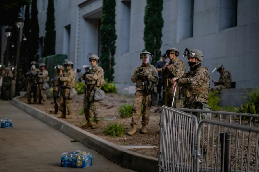 people in military fatigues stand by the side of a street