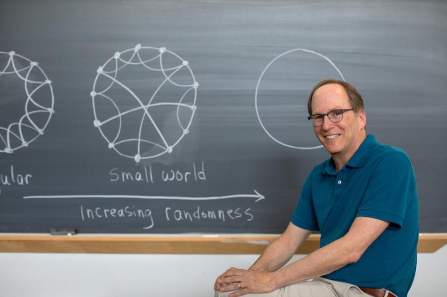 Person sitting in front of a chalk board that has circular "smal world" diagrams on it