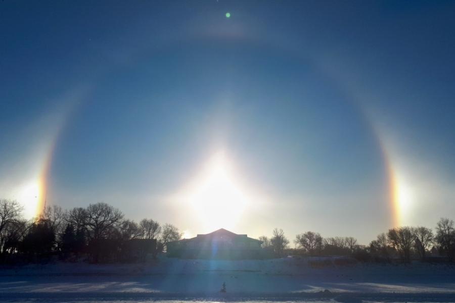 In the sky, a perfect half circle appears around a rising sun with two bright "sun dogs" on either side