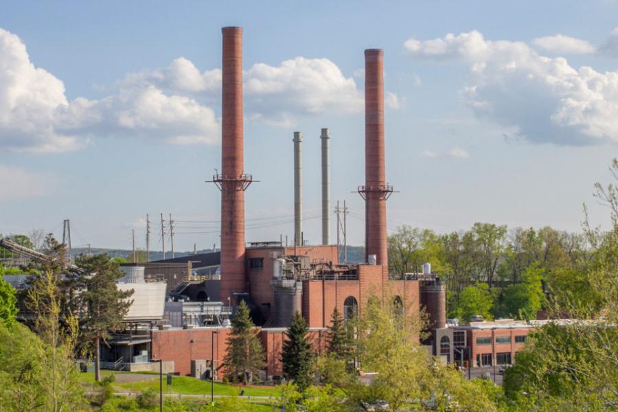 A brick building, the Combined Heat and Power Plant at Cornell, amid an idyllic landscape on a beautiful spring day