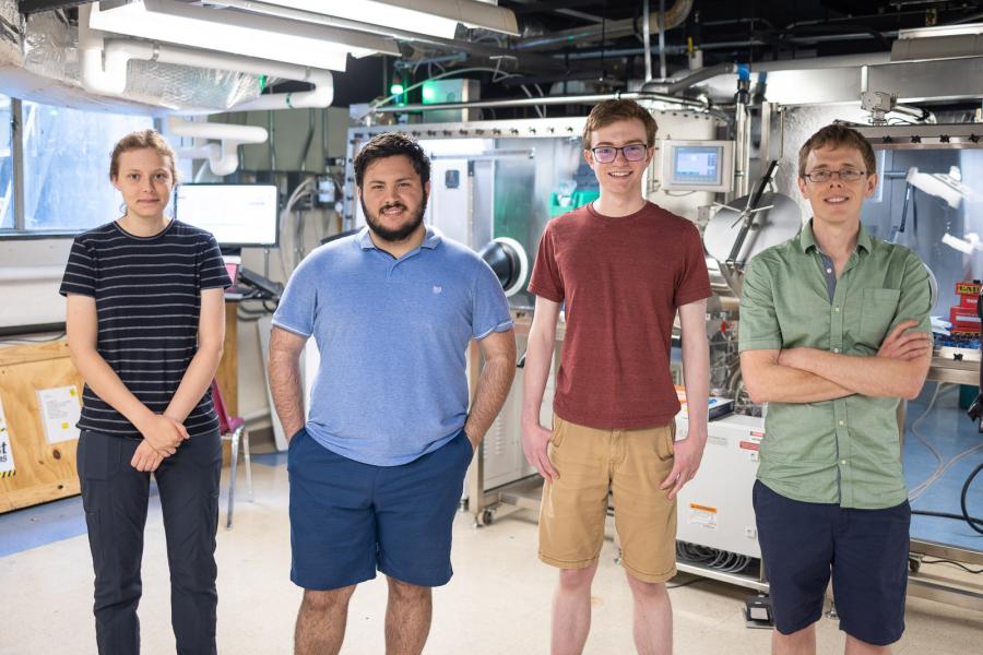 Three students, a young woman and two young men, sit next to professor Musser in his lab.