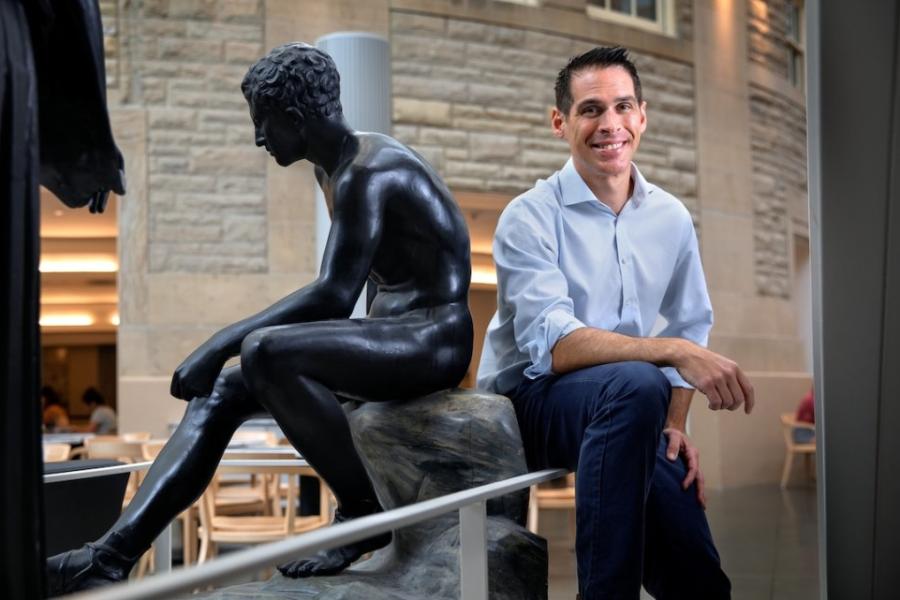 Person sitting casually back to back with a statue of a seated human figure carved from black stone
