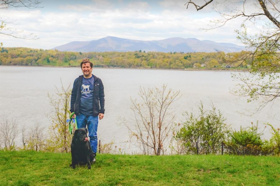 Person standing with a dog on the bank of a river