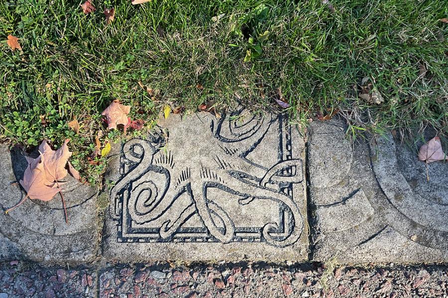 Close up of a paving stone carved with an octopus, next to grass