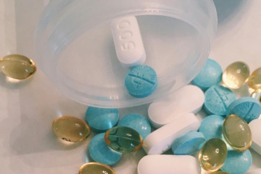 close-up of pillls of sevreal sizes and colors, spilling out of a bottle