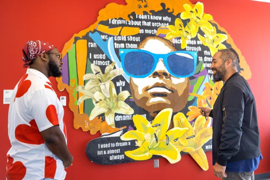 Two people stand with a colorful mural between them