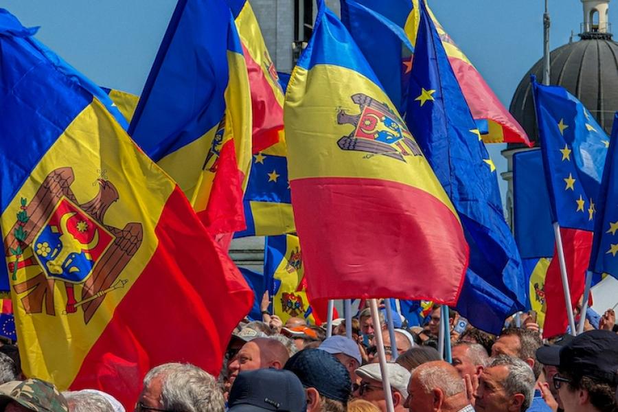 Blue sky, stone spire with a cross on top, people holding red, yellow and blue flags