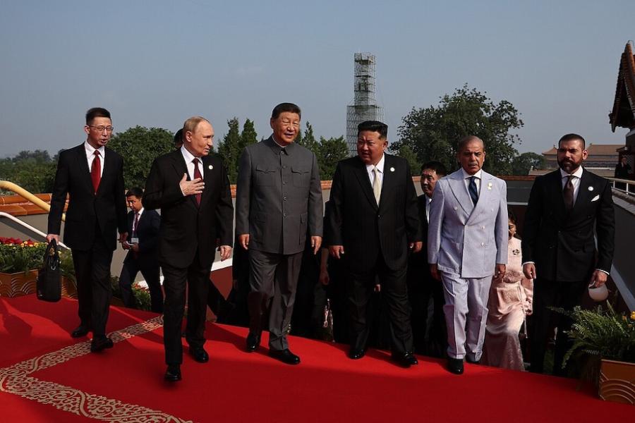 Six people in suits walk abreast up a red carpet, conversing