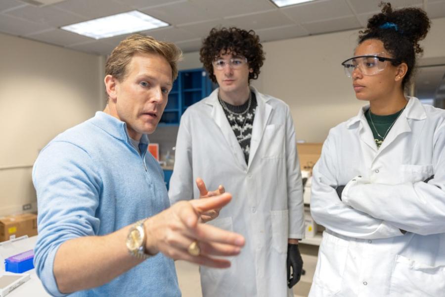 three people; two in lab coats, looking at the third, who is pointing instructively