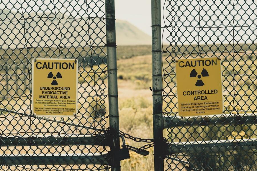 Chain link fence with yellow warning signs: CAUTION, UNDERGROUND RADIOACTIVE MATERIAL AREA