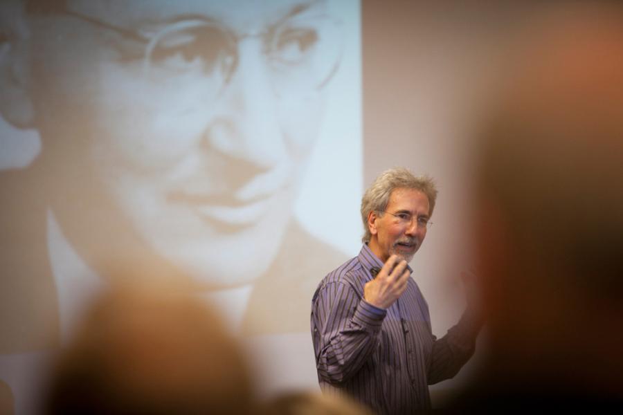 person speaking with images presented behind him