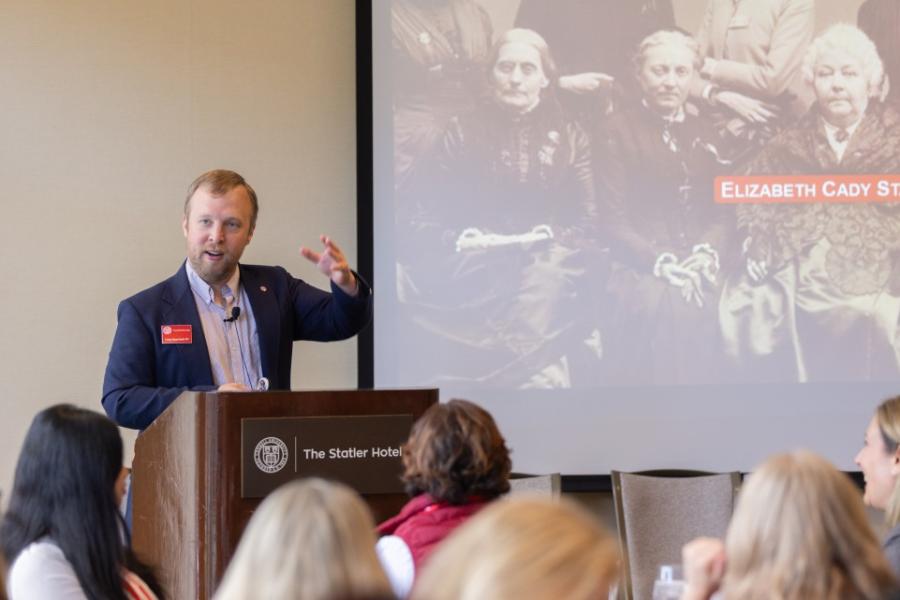Person speaking at a lecturn with a black and white photograph displayed behind