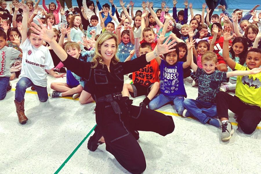 Person in black jump suit poses in front of a crowd of excited children