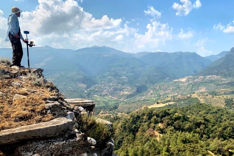 Person standing on a rocky hill, looking out over a huge, green plain