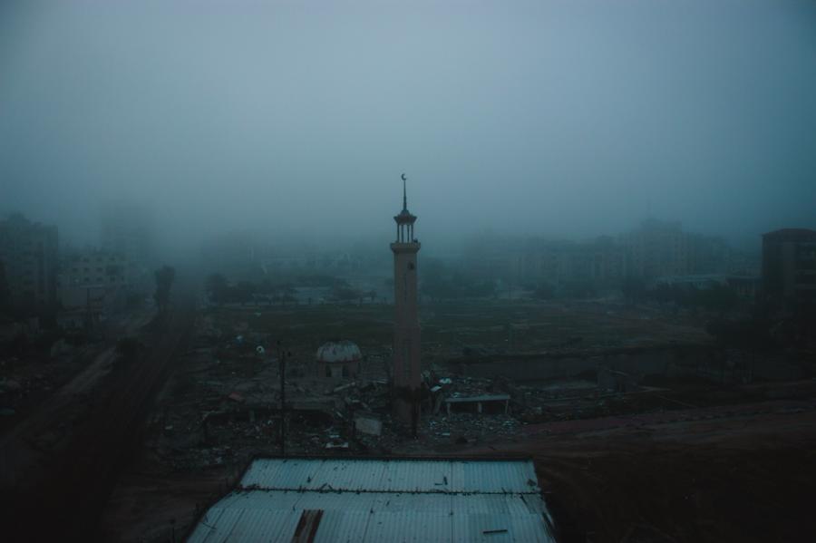mosque spire rises in fog over a war-damaged street