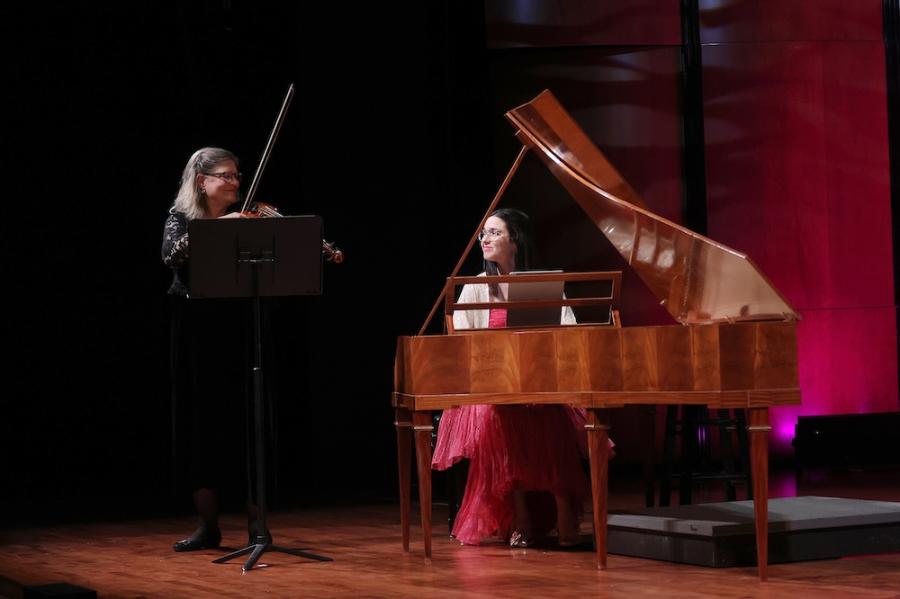 A person stading plays a stringed instrument with a person playing a piano 