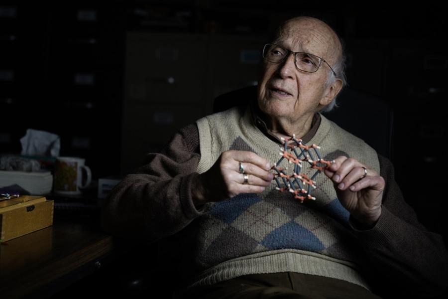 Artistic portrait of a person in argyle pattern sweater vest holds a small model of a molecule and looks pensive