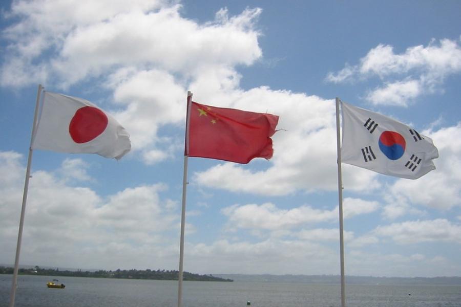 Flags of east Asia on poles near a body of water. Blue sky behind them
