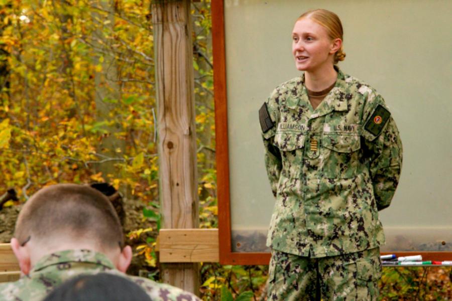 Person in military fatigues standing in front of others, speaking