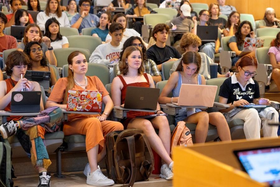 Dozens of college students sit at attention in an auditorium with tiered seating