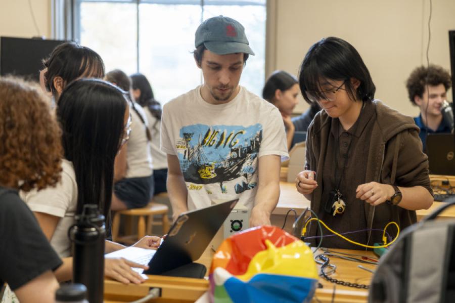 About five students cluster around a table full of equipment in an introductory physics lab