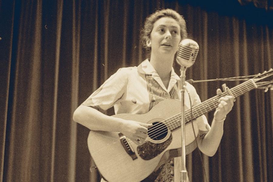 Black and white historic photo of a person playing a guitar and singing into a microphone