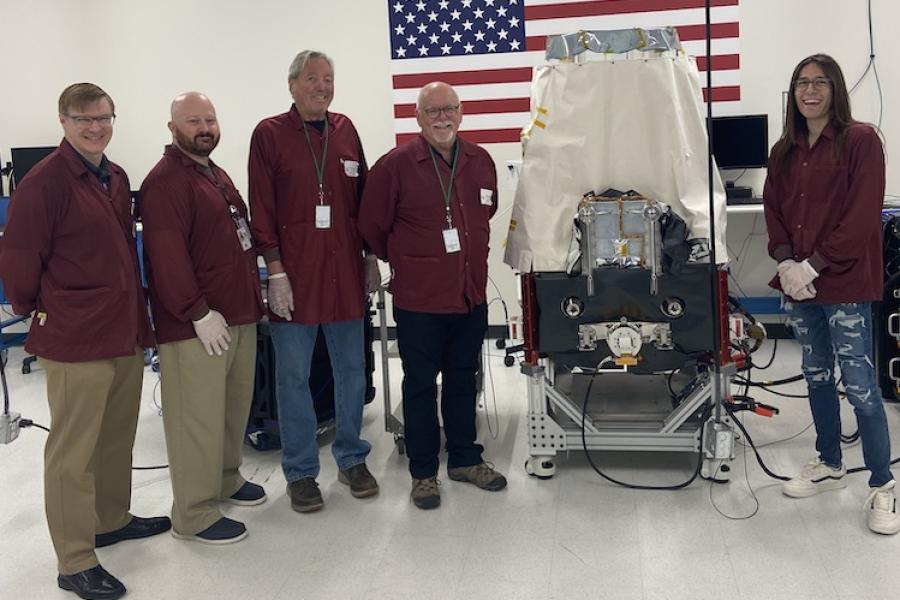 Five people stand together with a piece of equipment the size of a refrigerator