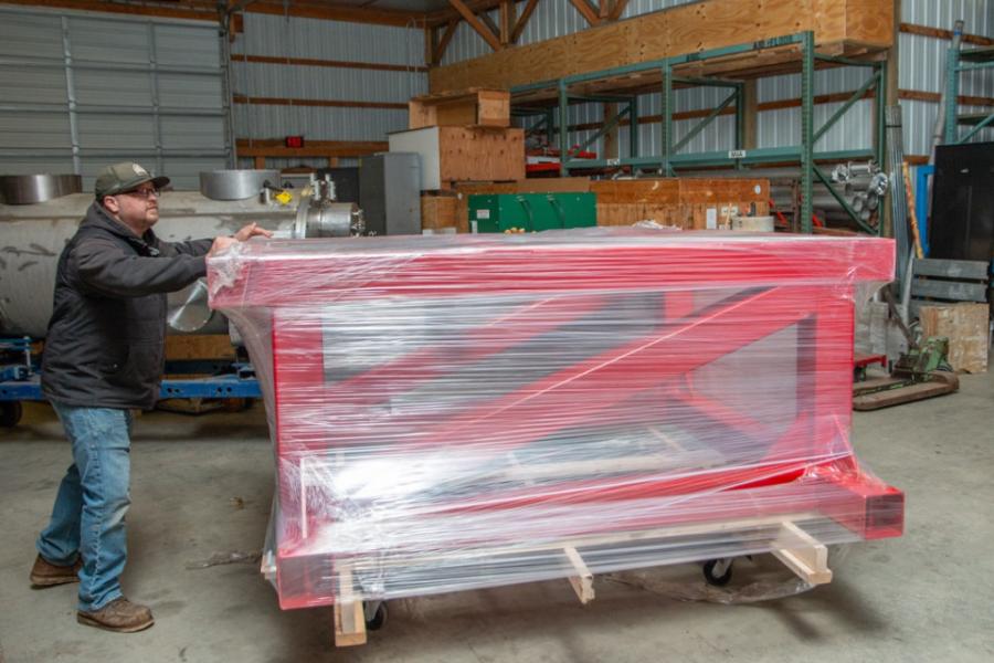 Person pushing, on a dolly, a large red frame wrapped in plastic