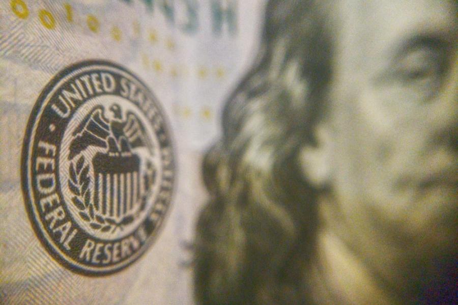 Circle on textured paper that says 'Federal Reserve'; an extreme close up of a one-dollar bill, US