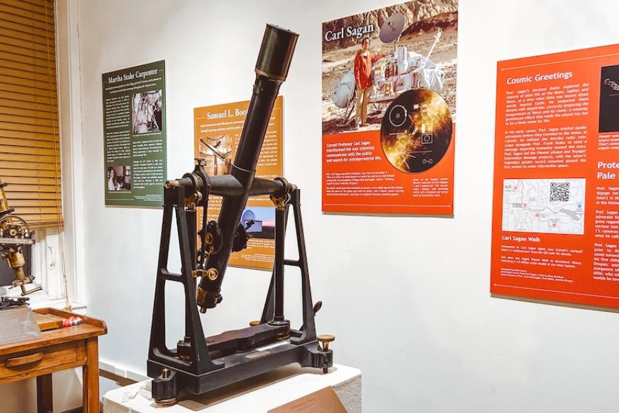 A small telescope on a pedestal with several posters in the background