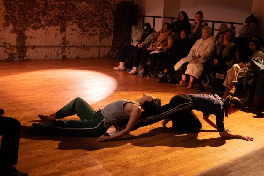Two dancers lean on each other while performing moves close to the floor in front of an audience
