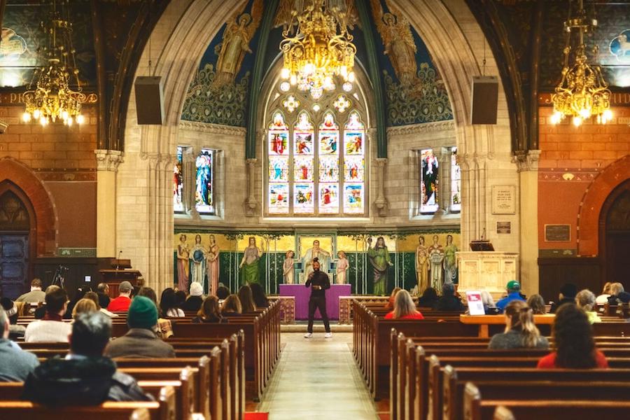Colorful interior of a chapel with a vaulted ceiling; people sit in the pews facing a person speaking at the front