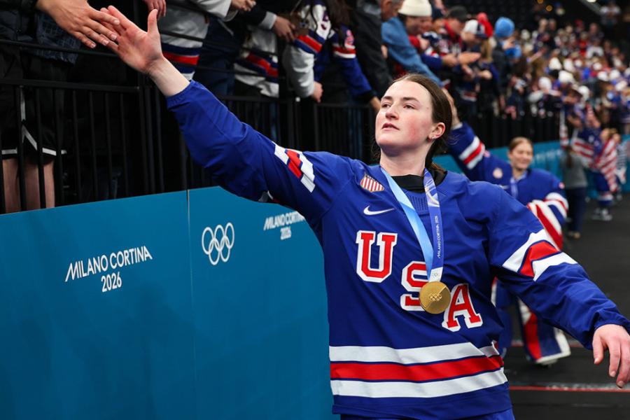 Person in a blue USA jersey reaches up to slap hands with a member of the crowd, celebrating