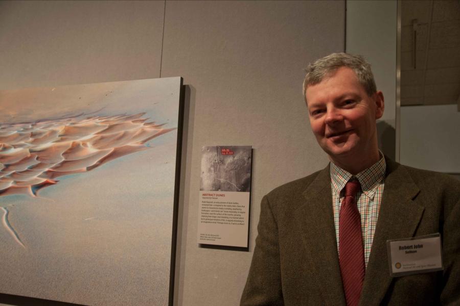 Robert Sullivan in suit and tie standing next to a poster hanging on the wall showing the ruffled surface of Mars.