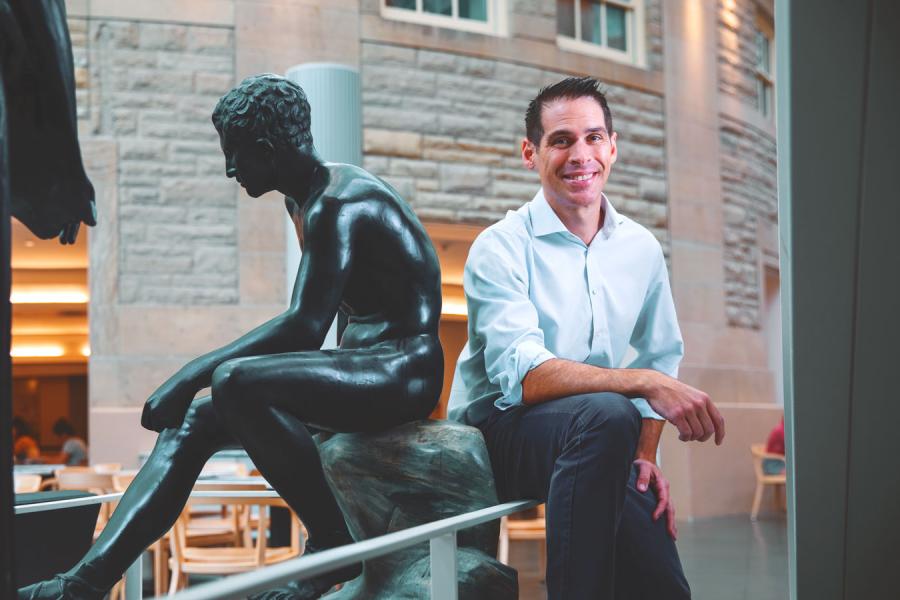 Person smiling next to a sculpture of a person sitting