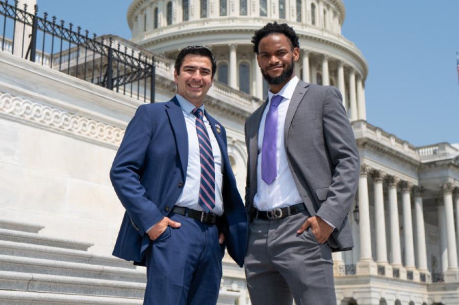 Two people in suits standing in front of the recognizable white dome of the US Capitol Building