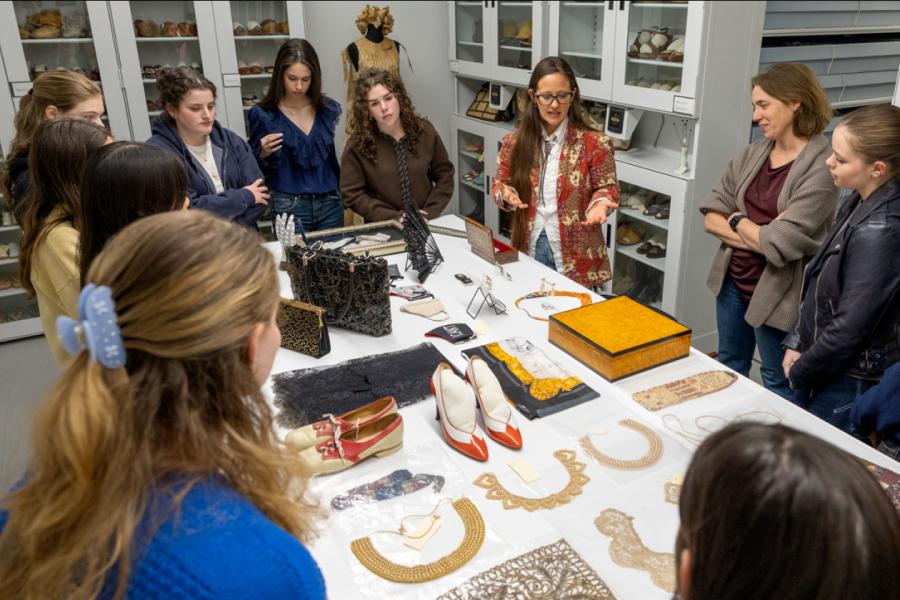 Several people clustered around a large table, on which shoes, handbags, boxes and collars are displayed