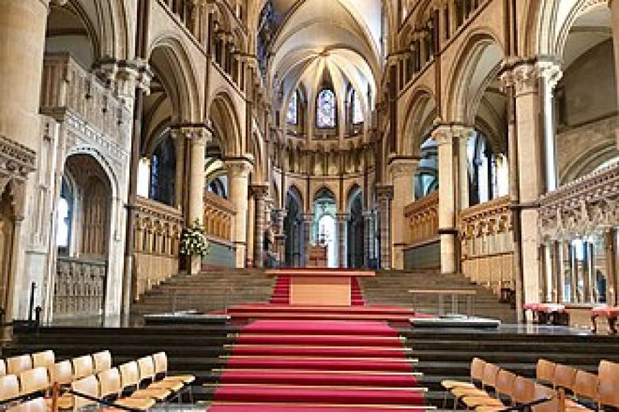 Columns and arches form the walls, with a red carpet leading up to the alter in this image of the interior of the cathedral 