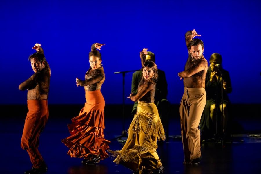People on a stage, dancing dramatically in yellow and orange costumes