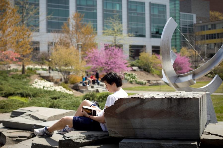 Person reading a book while sitting on a large rock outdoors