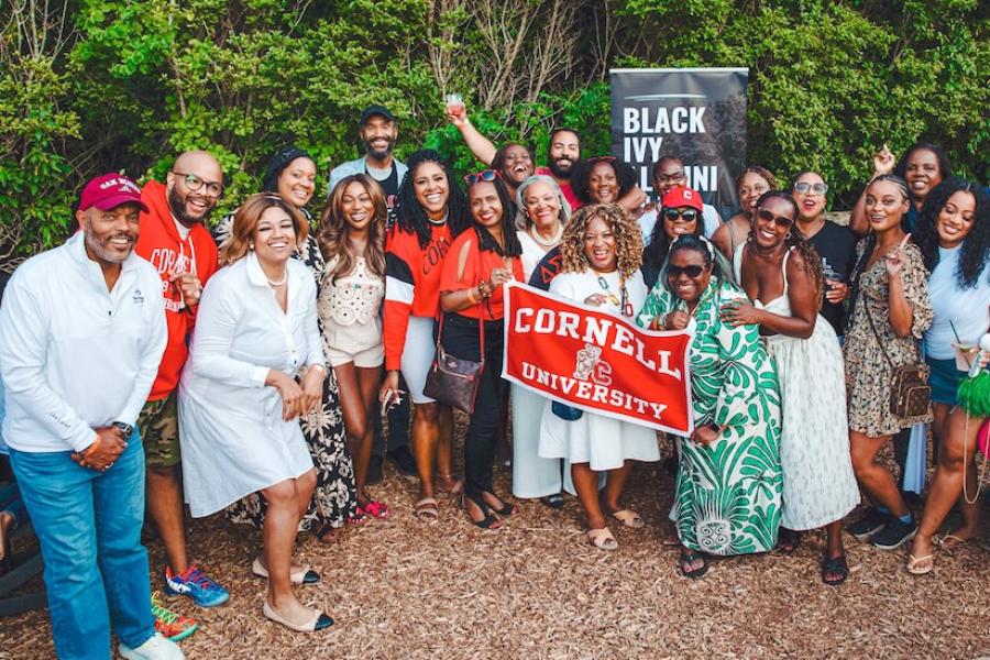 A few dozen people in summer fashions cluster together with a Cornell University banner