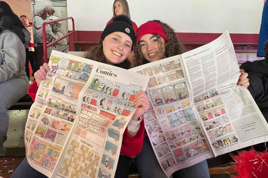 two people holding newspaper at a hockey game