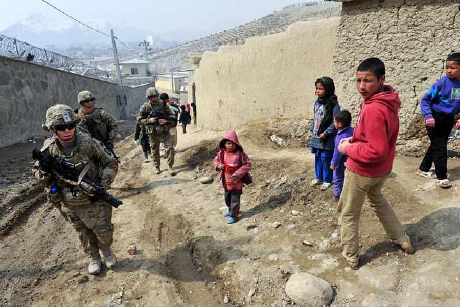 Armed soldiers walk up an incline alongside five children in colorful clothing. It's peaceful