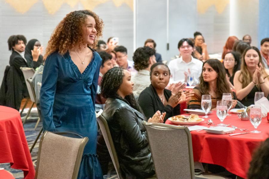 Person walking past a table where others sit, looking on and applauding