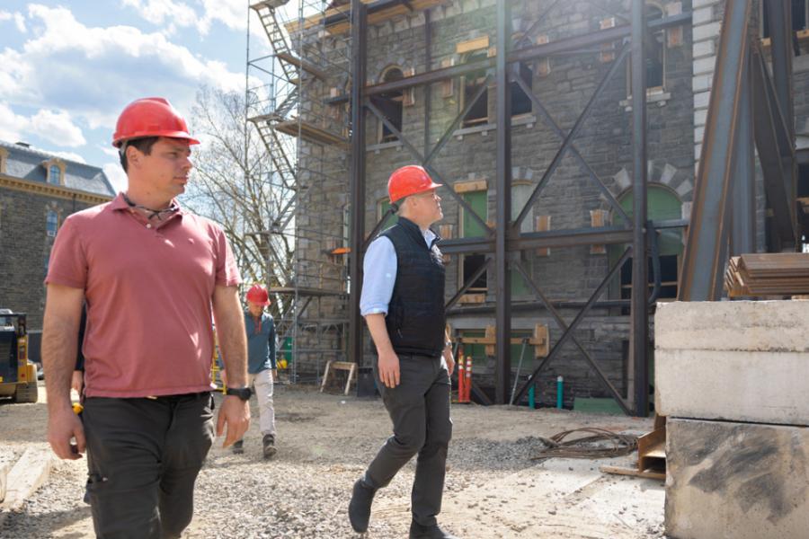 Two people in red hard hats walk through a building construction site
