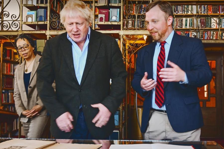 Two people discuss papers laid out on a table while a third looks on from the left