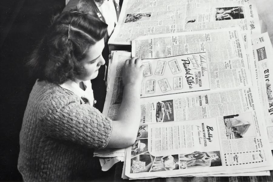 Historic black and white image of five people reading newspapers together at a table