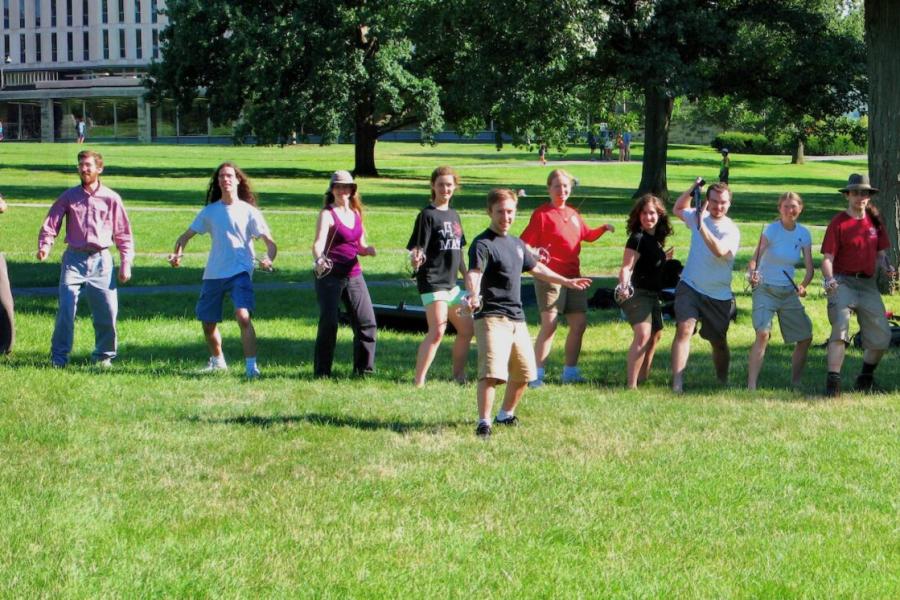 Several people pose imposingly with swords on the green lawn of Cornell's Arts Quad