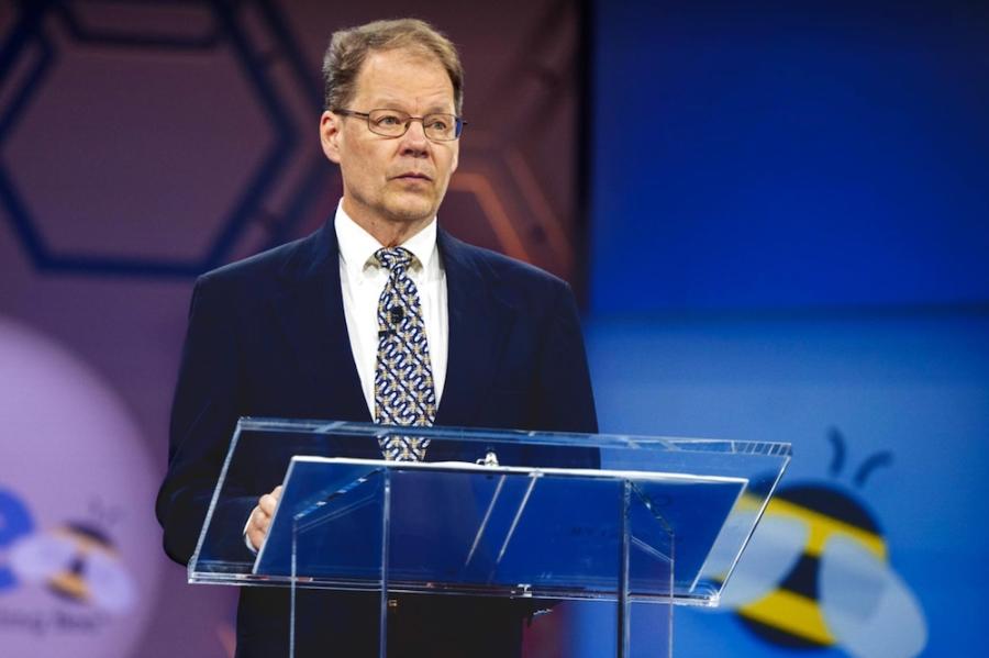 Person standing at a podium, looking serious